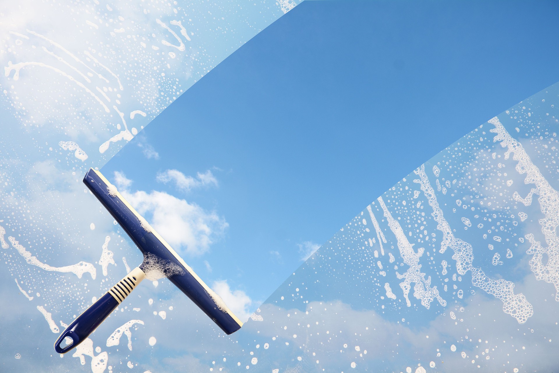 Caoutchouc raclette nettoie une fenêtre savonnГ et efface une bande de ciel bleu avec des nuages, la notion de transparence ou de nettoyage de printemps, espace copie en arrière-plan
