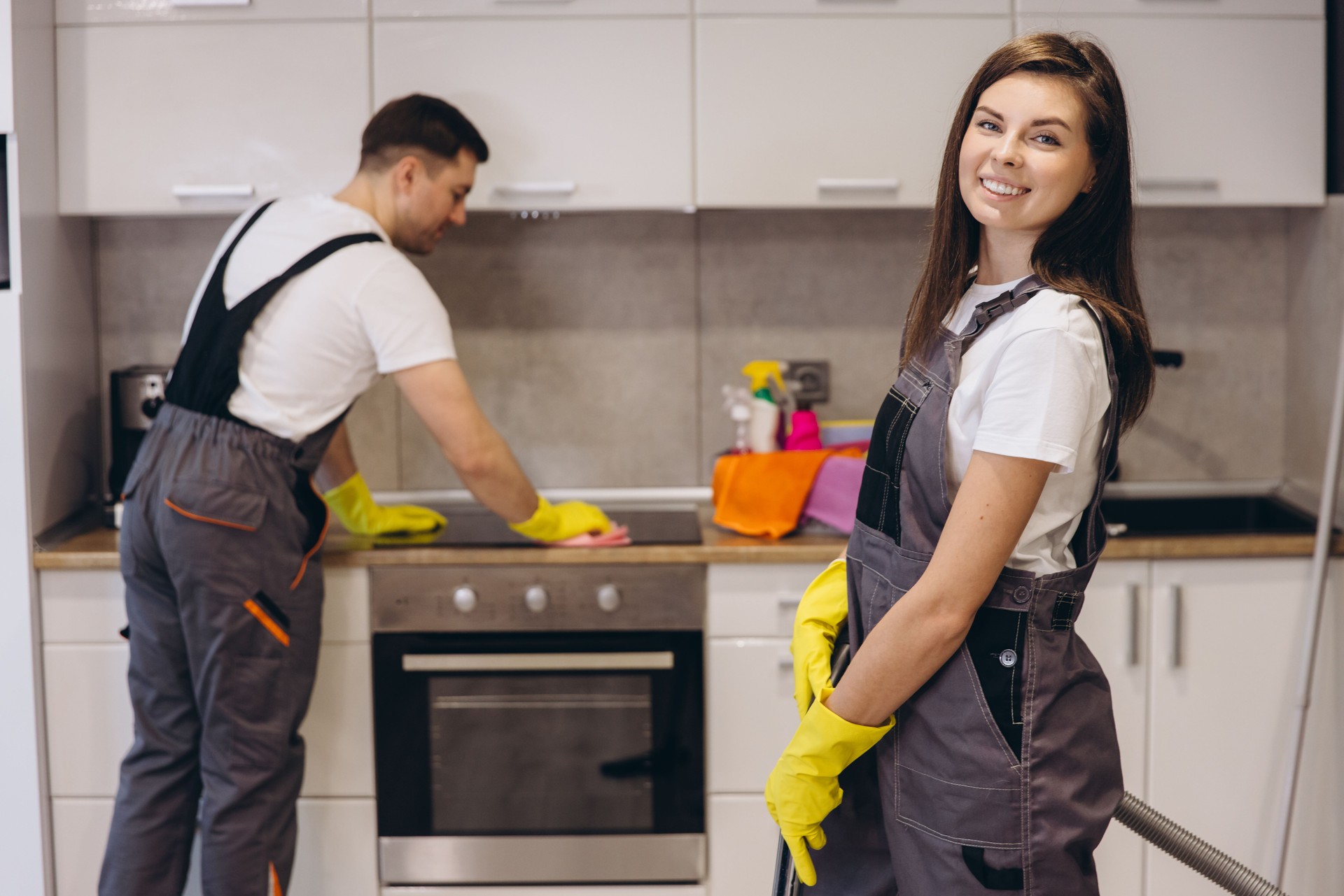 Employés de l’entreprise de nettoyage nettoyant les surfaces de la cuisine et souriants